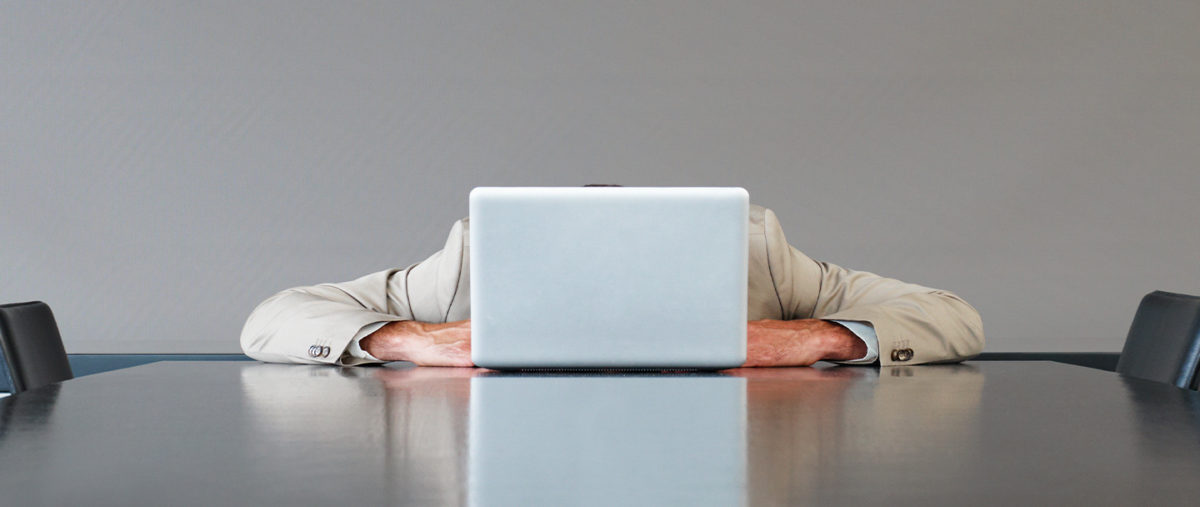 Man sitting at a conference table with his head buried into his laptop